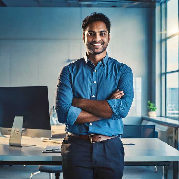 Compliance manager standing arms crossed at his desk with a desktop computer